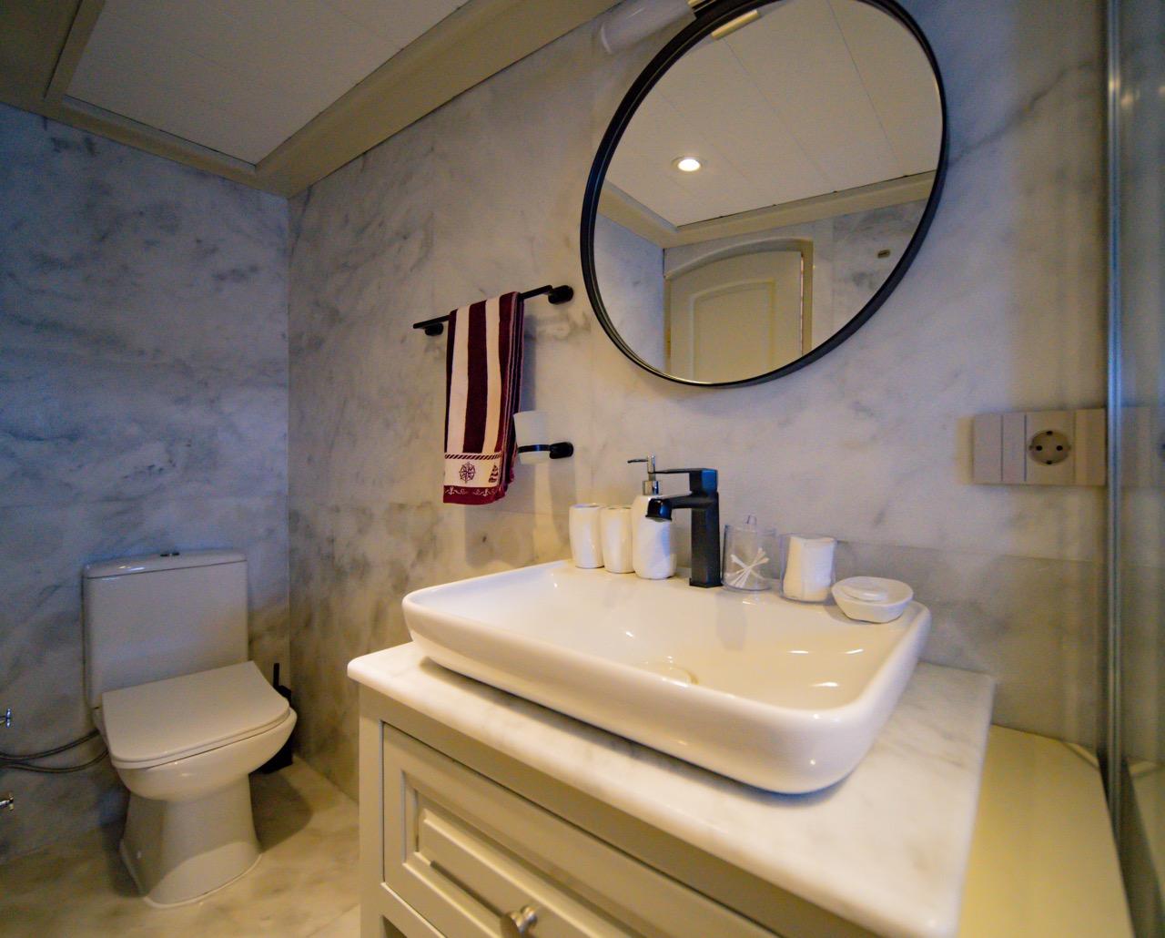 modern yacht bathroom featuring white vessel sink, round black-framed mirror, and marble walls