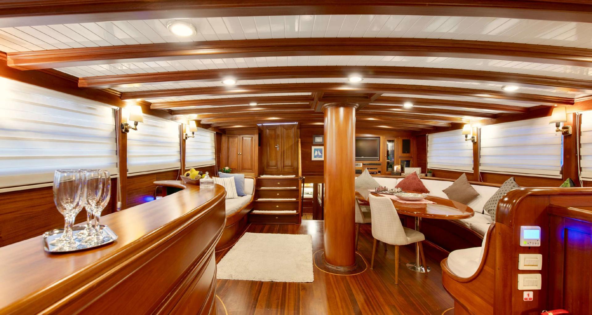 yacht salon with curved banquette seating, dining table, wooden ceiling beams and windows