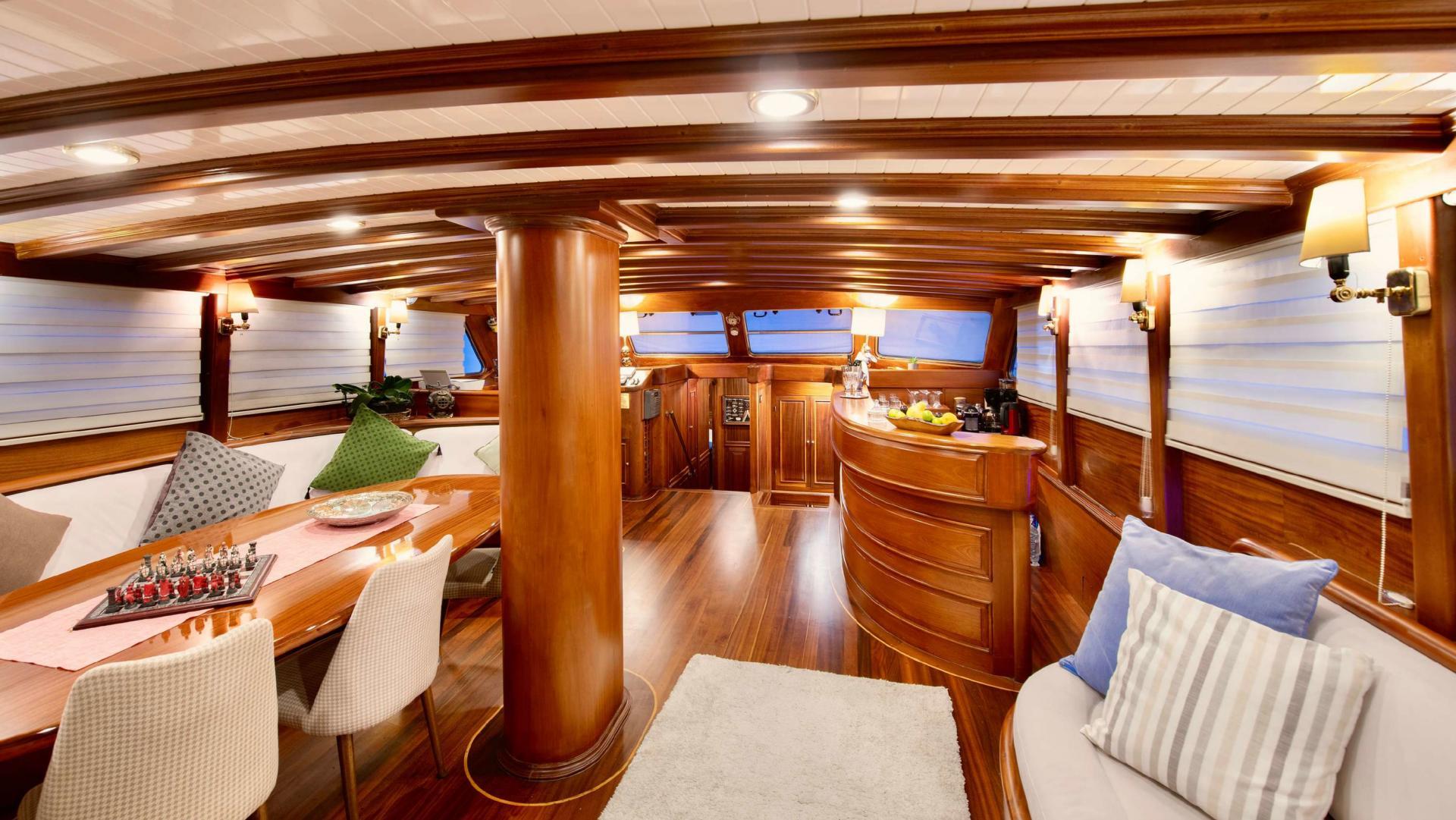 yacht main salon with dining table, galley kitchen, wooden beams and seating area