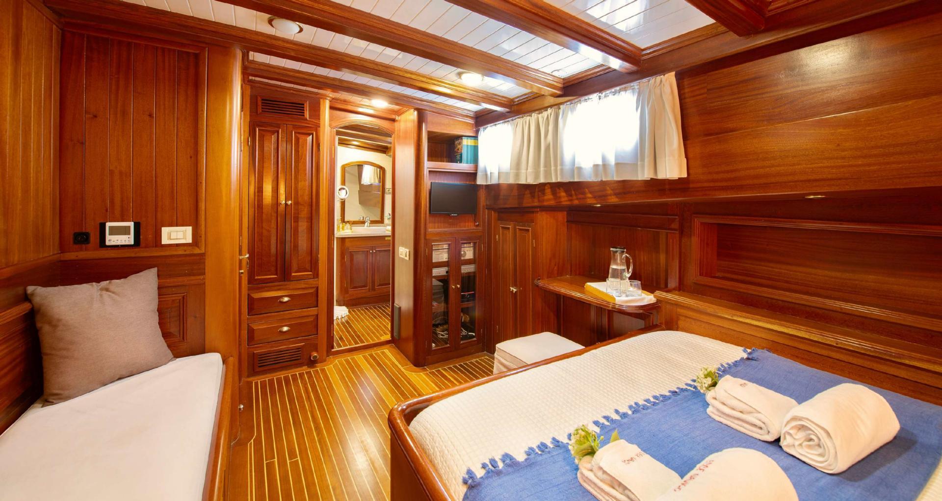yacht cabin interior featuring bed with blue runner, teak paneling, built-in wardrobes and seating area
