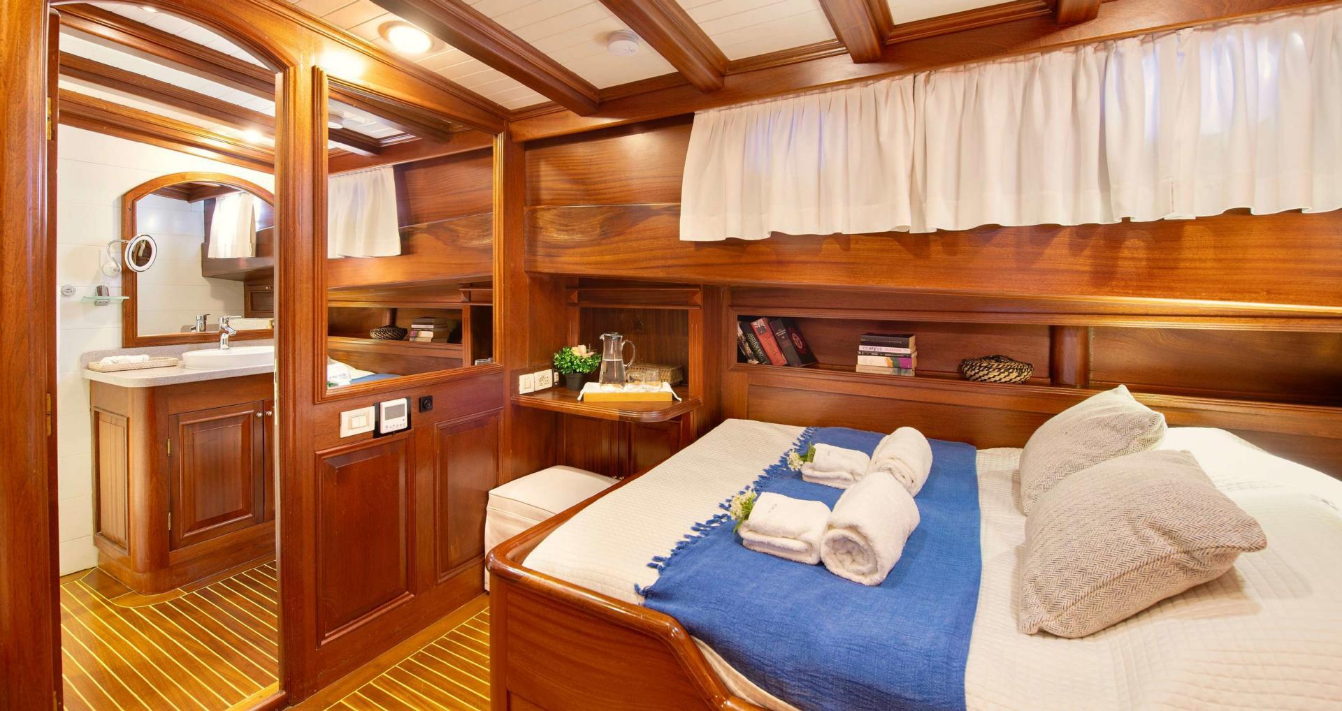 yacht guest cabin featuring double bed with blue runner, built-in storage shelves, and adjoining en-suite bathroom