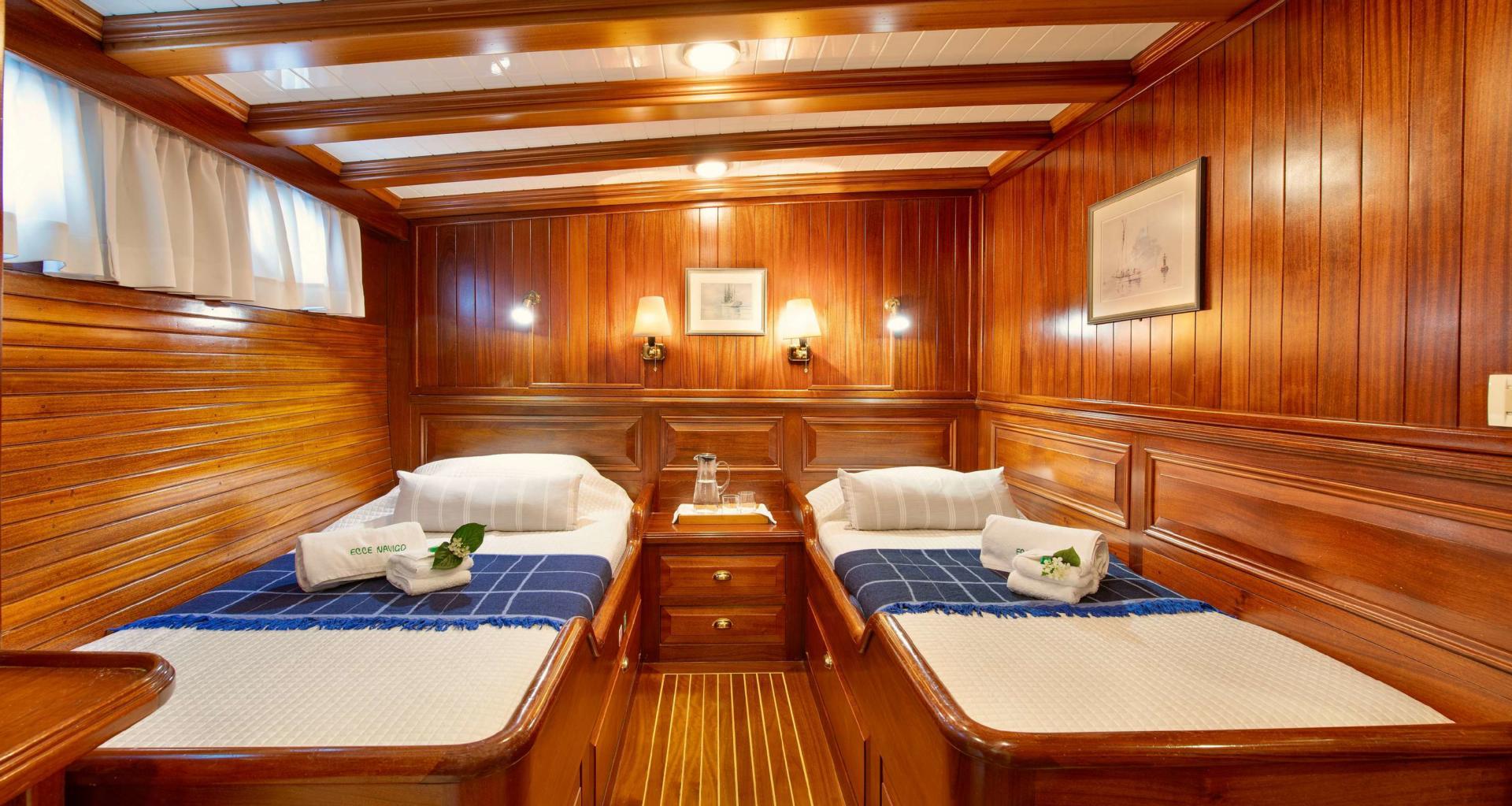 twin guest cabin featuring two single beds with blue runners and classic teak wood paneling