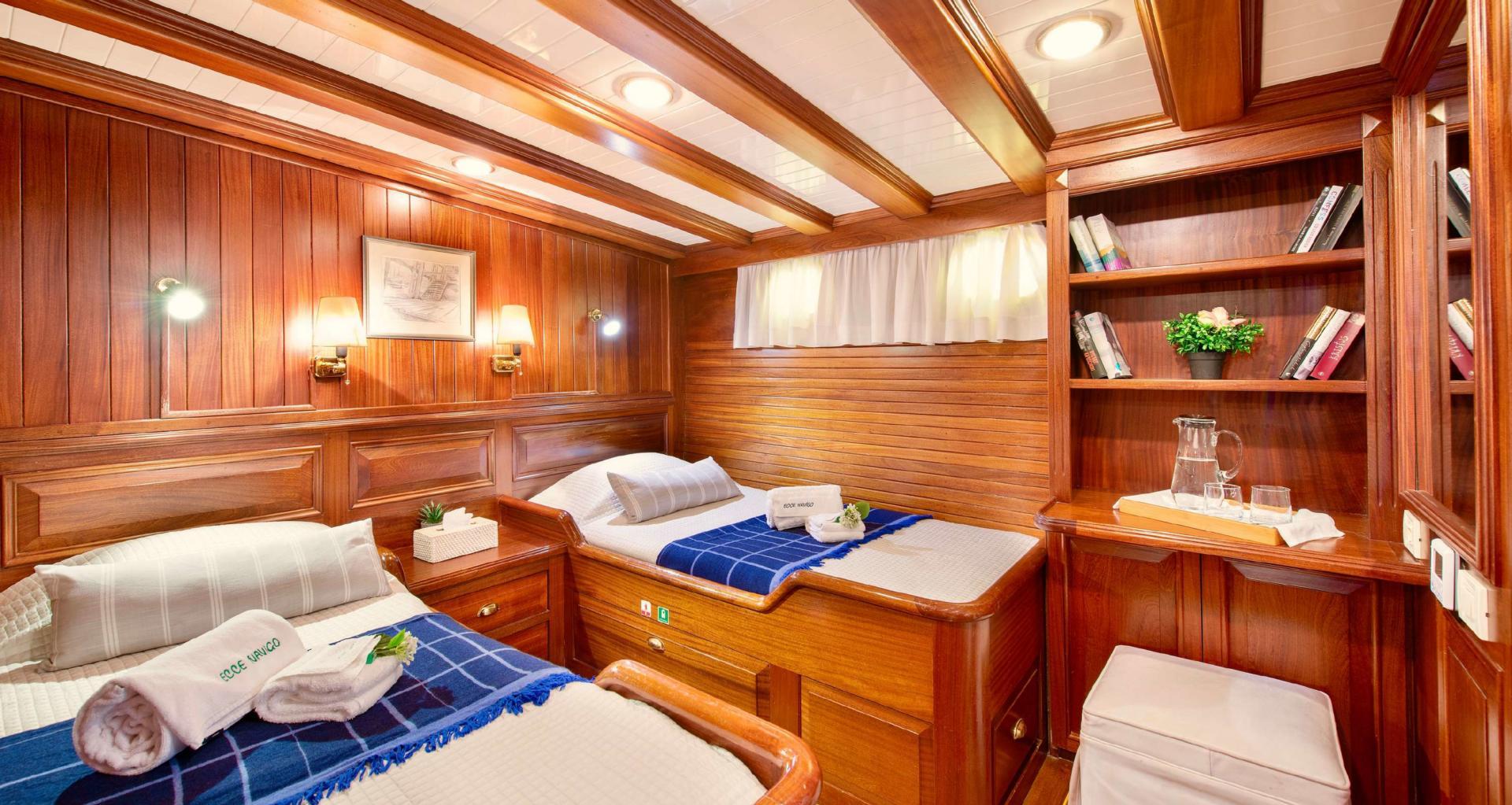 yacht twin cabin with two single beds, wooden paneling, built-in shelving and porthole window