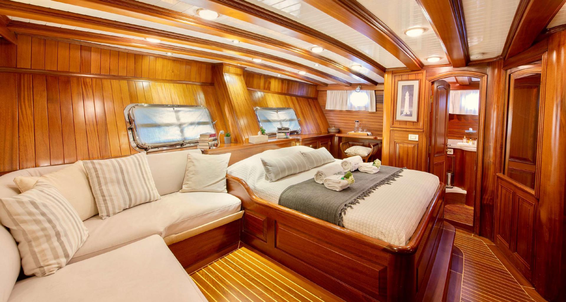 luxury yacht master cabin featuring king bed, cream upholstered seating area and teak woodwork