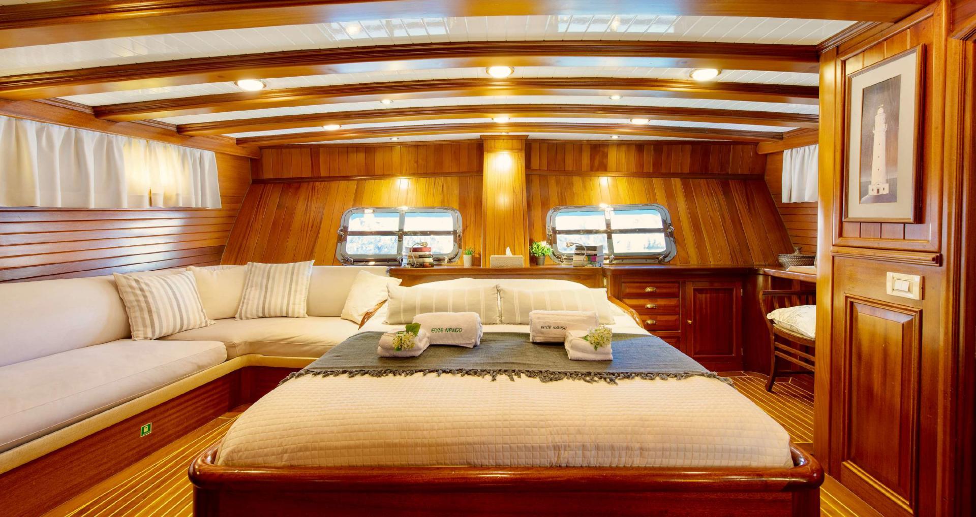 yacht master cabin interior with double bed, curved seating, portholes and wood paneling