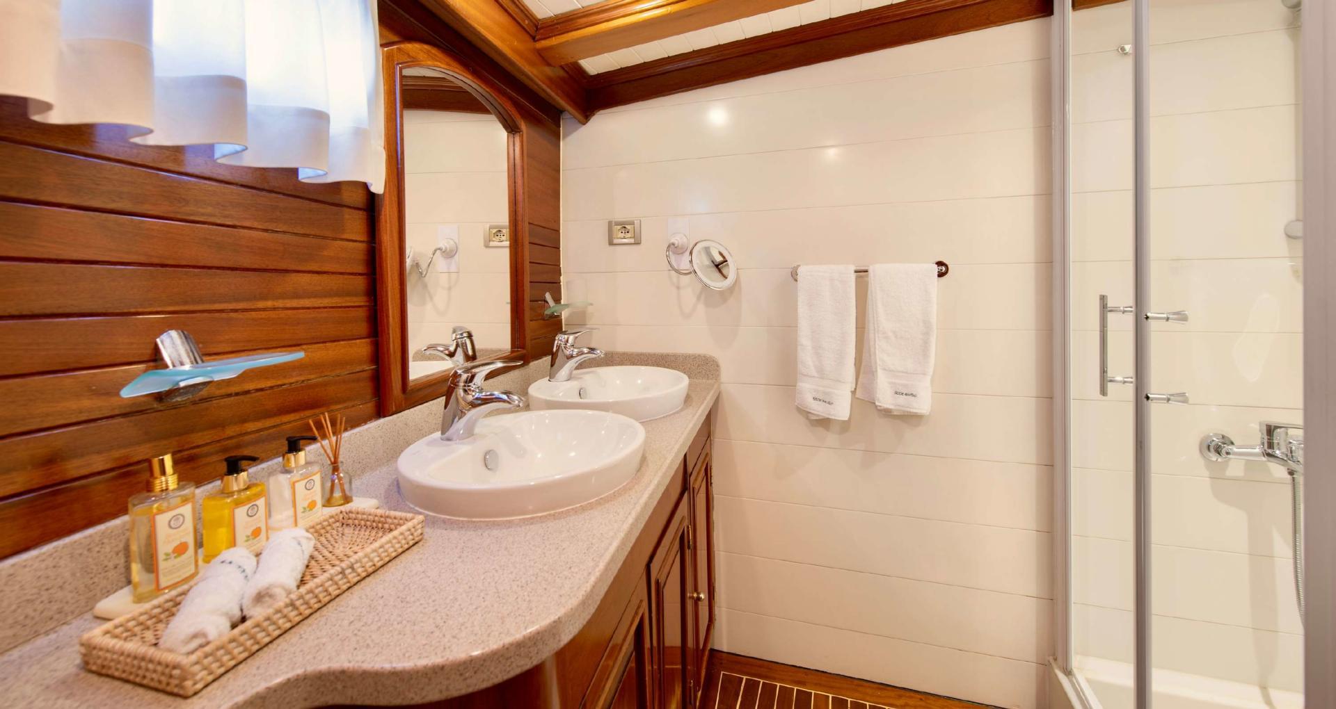 yacht bathroom featuring dual vessel sinks, marble countertop, walk-in shower, and wood paneling