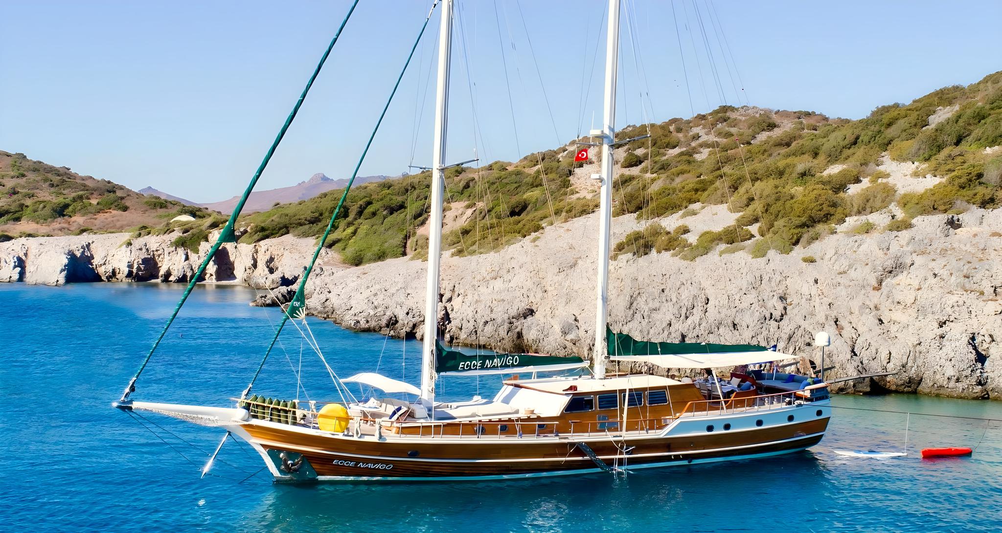 Traditional wooden gulet Ege Navigo anchored in turquoise Mediterranean bay with rocky coastline