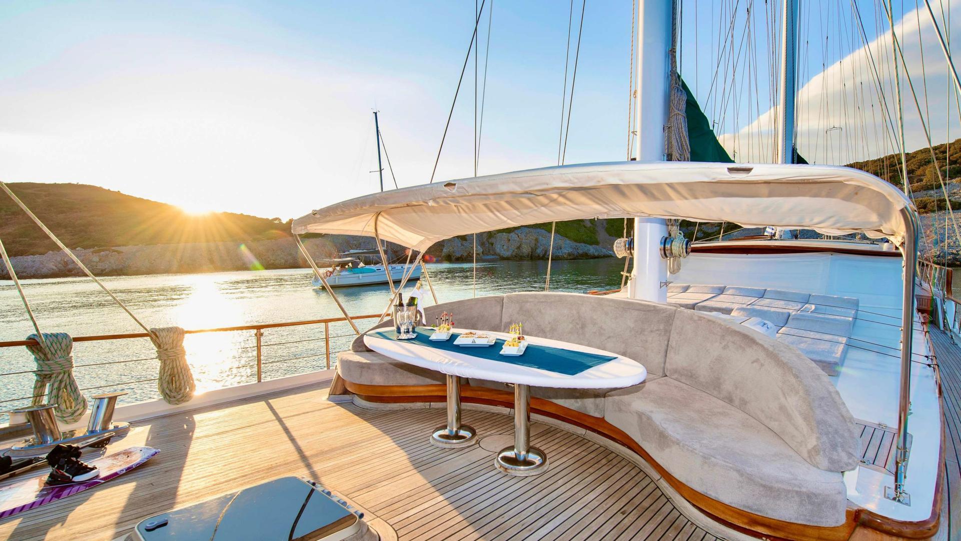 gulet aft deck with curved upholstered banquette seating, oval table and white canopy at sunset