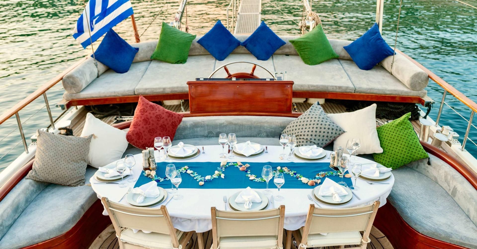 gulet aft deck with formal dining table, U-shaped seating, colorful cushions and helm station