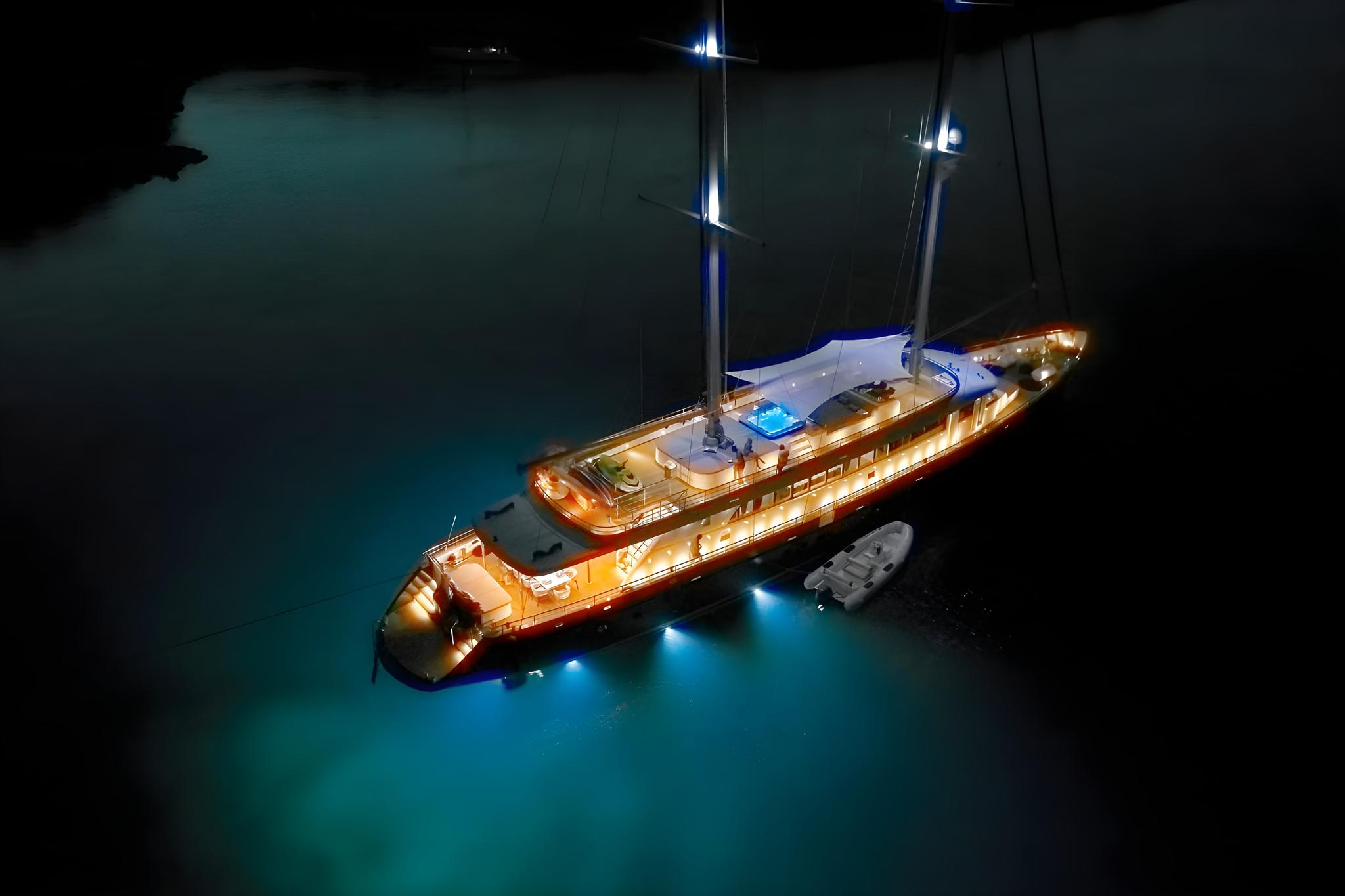 luxury sailing yacht with golden deck lighting anchored in turquoise waters at night