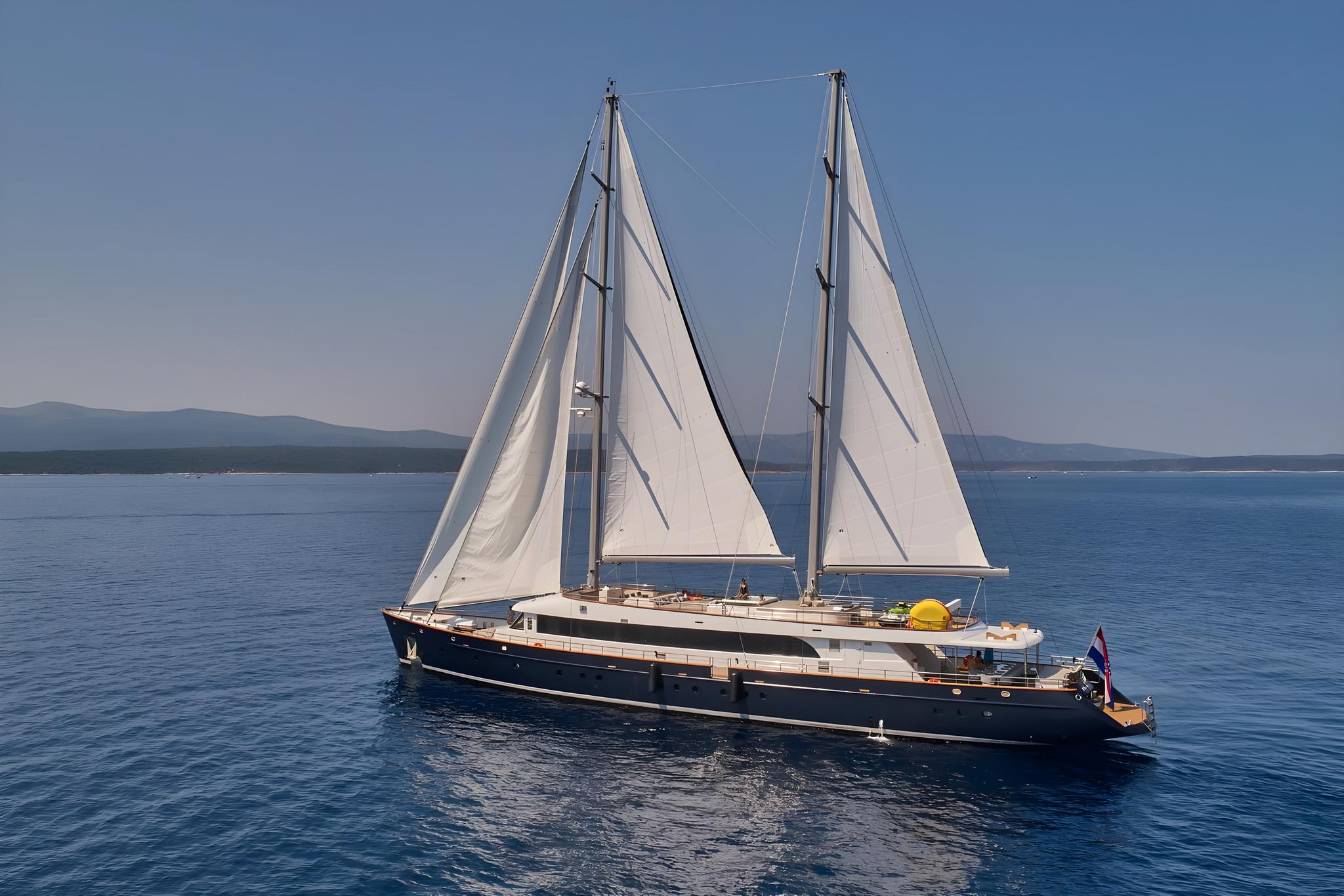 Dark blue hulled sailing yacht with white sails on calm blue waters