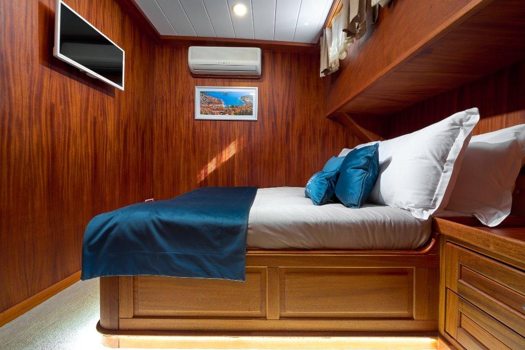 luxury yacht cabin with teal bedding, wood paneling, TV and air conditioning