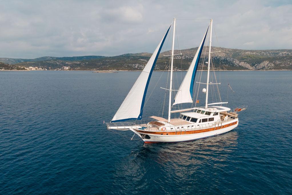 White gulet sailing with blue-trimmed sails in Mediterranean waters aerial view