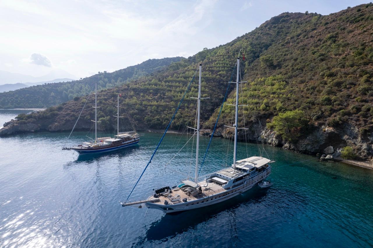 aerial drone shot of two traditional gulets anchored in protected turquoise bay surrounded by forested hills