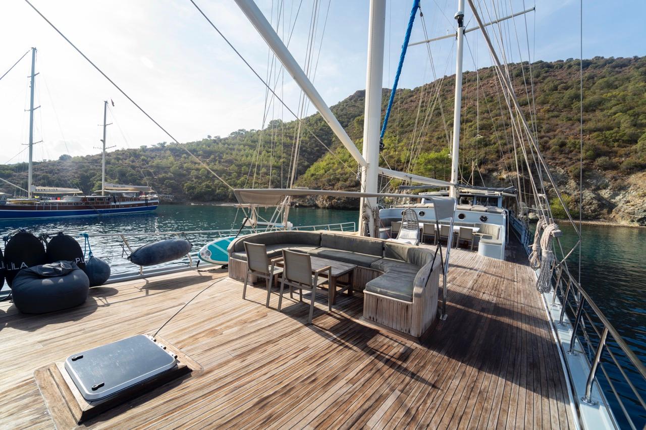 gulet aft deck with curved banquette seating, dining table and teak decking in secluded bay