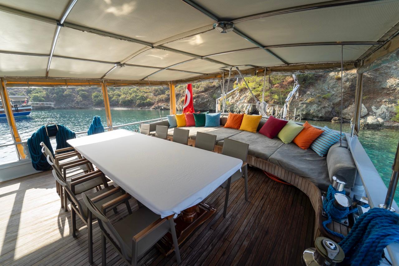 gulet aft deck with white dining table, grey chairs and colorful cushioned seating under awning