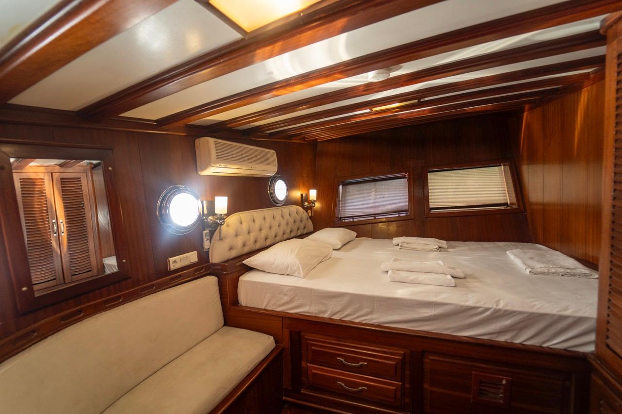yacht cabin interior with double bed, cream upholstered headboard, built-in seating and wooden paneling