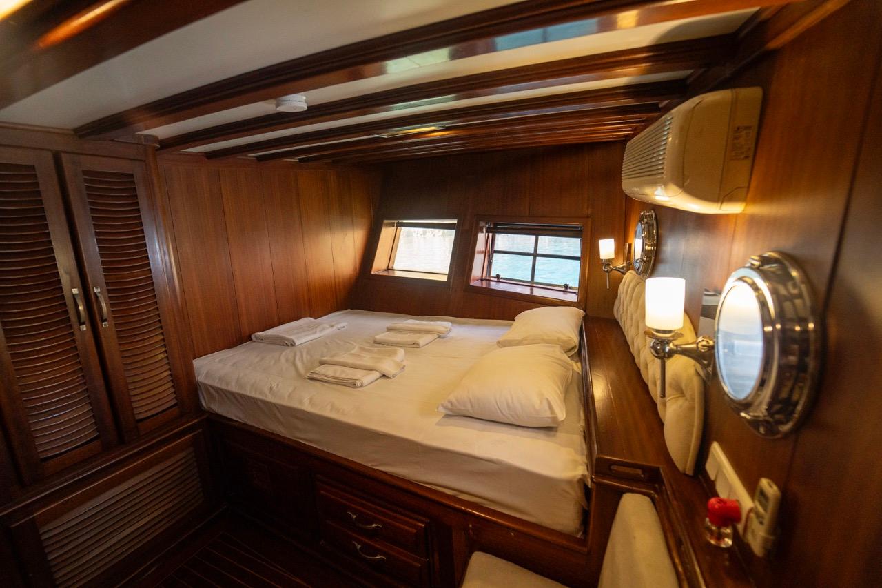 yacht guest cabin featuring double bed with white linens and two rectangular portholes