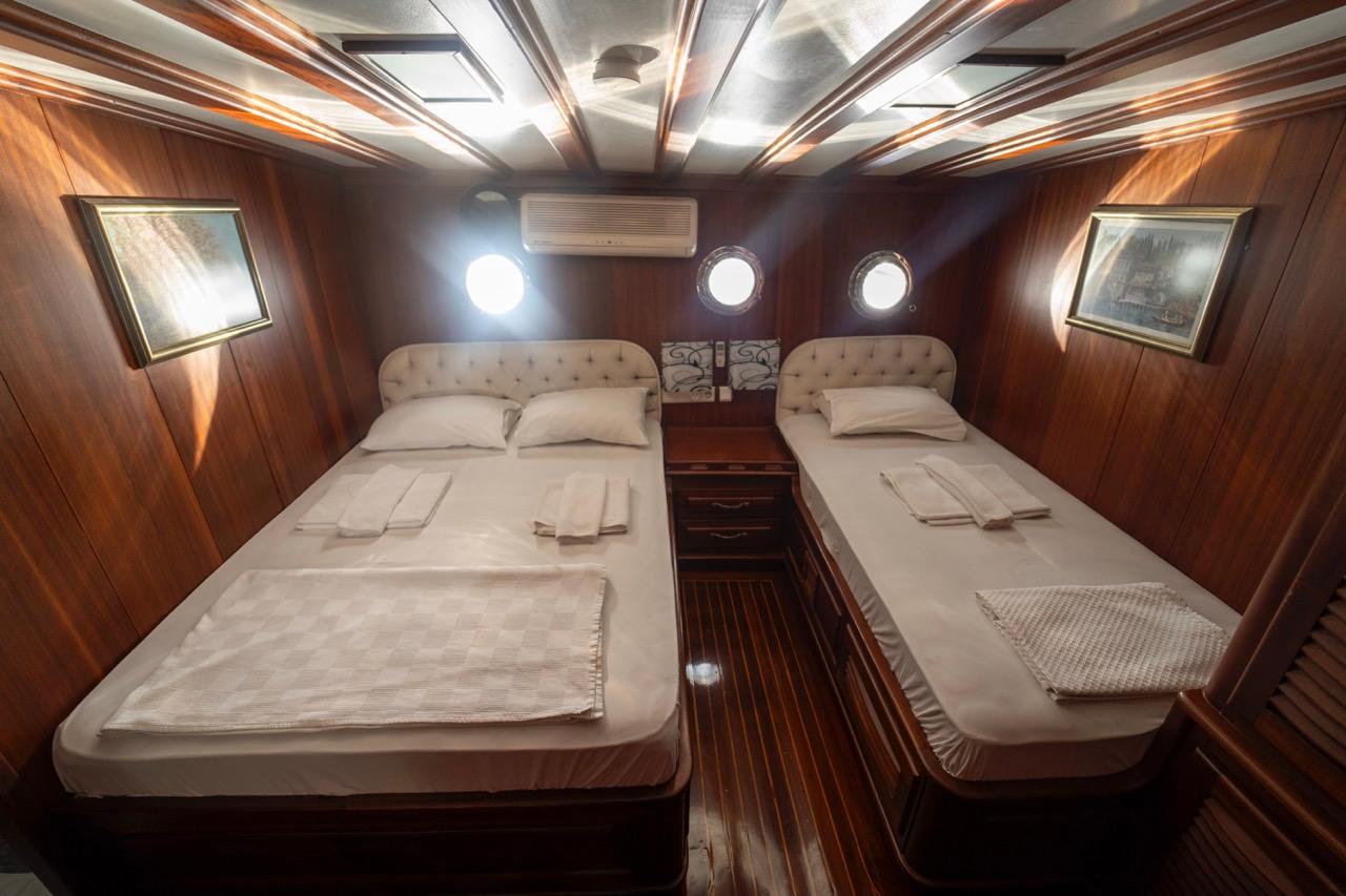 yacht twin cabin with two single beds, tufted headboards, three portholes and wood paneling