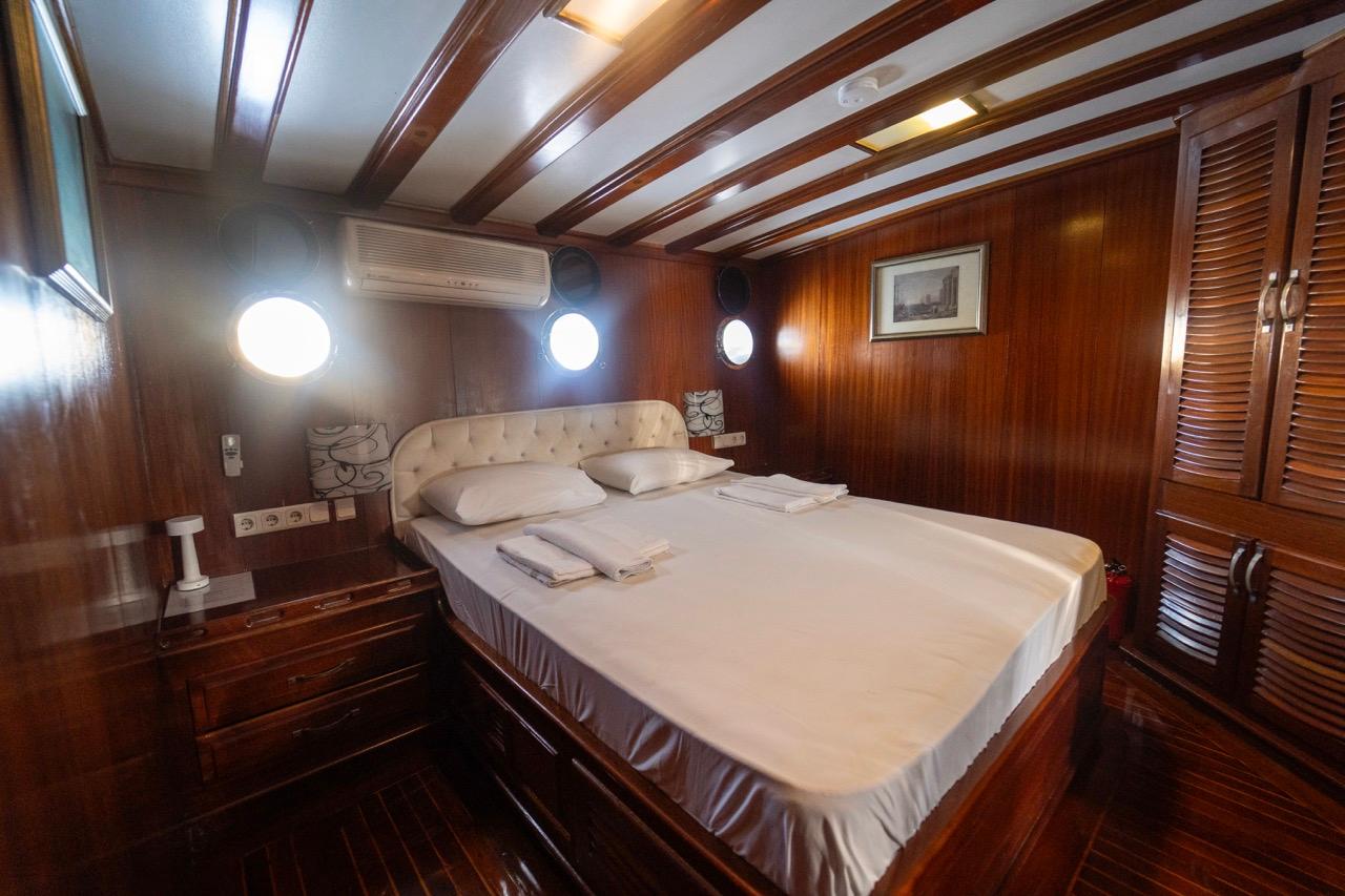 yacht guest cabin featuring double bed with white linens, wood paneling, portholes and built-in storage