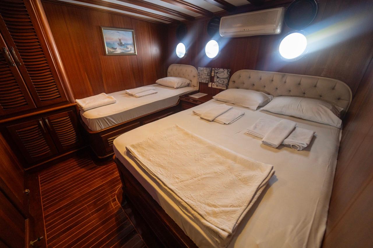 yacht guest cabin with two single beds, tufted headboards, and three round portholes