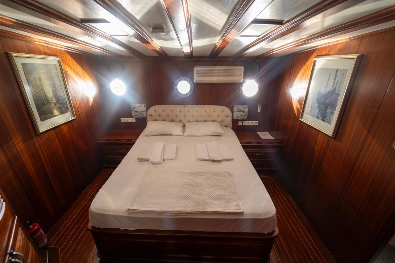 yacht guest cabin with double bed, cream upholstered headboard, wooden paneling and three portholes