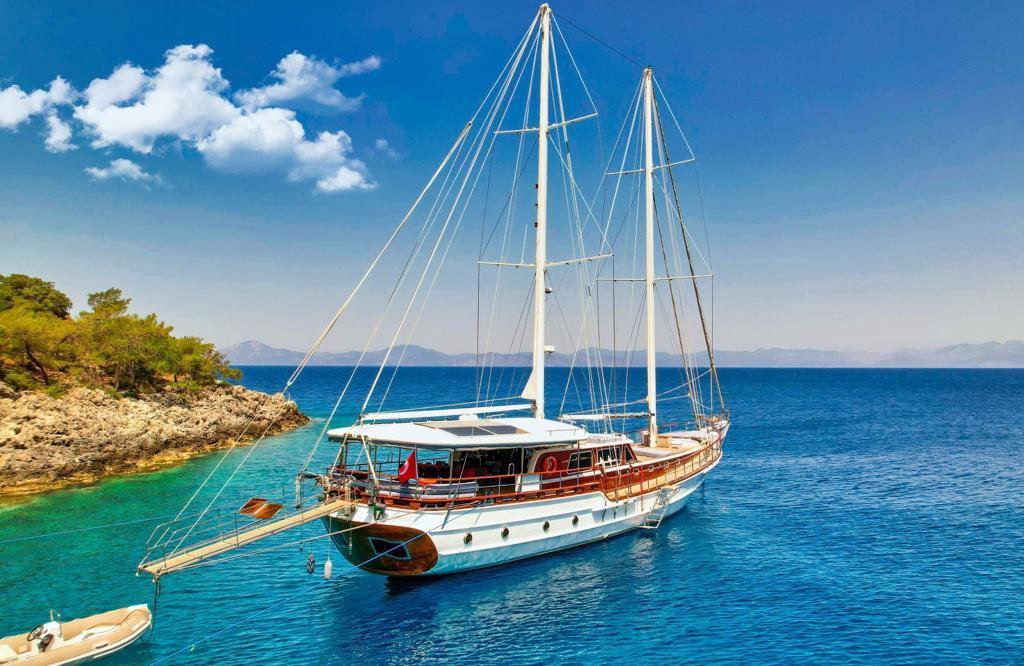white traditional gulet with two masts anchored in crystal clear turquoise waters near rocky coastline