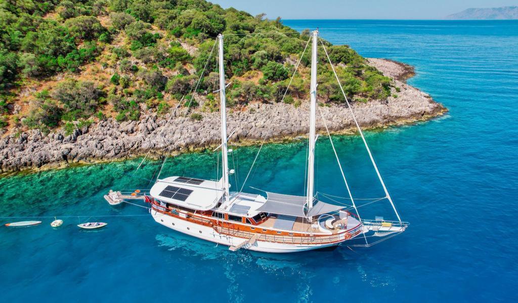 aerial view of traditional wooden gulet yacht anchored in crystal clear turquoise bay near rocky coastline