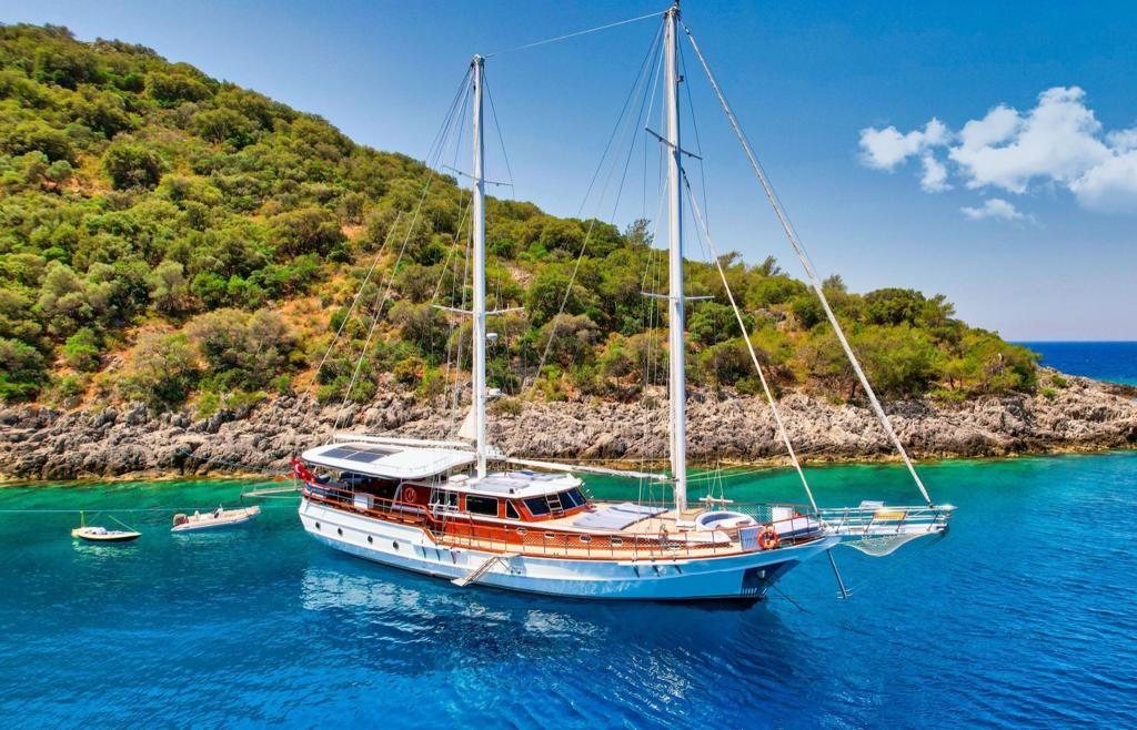 White traditional gulet with wooden trim anchored in crystal clear turquoise waters near forested coastline
