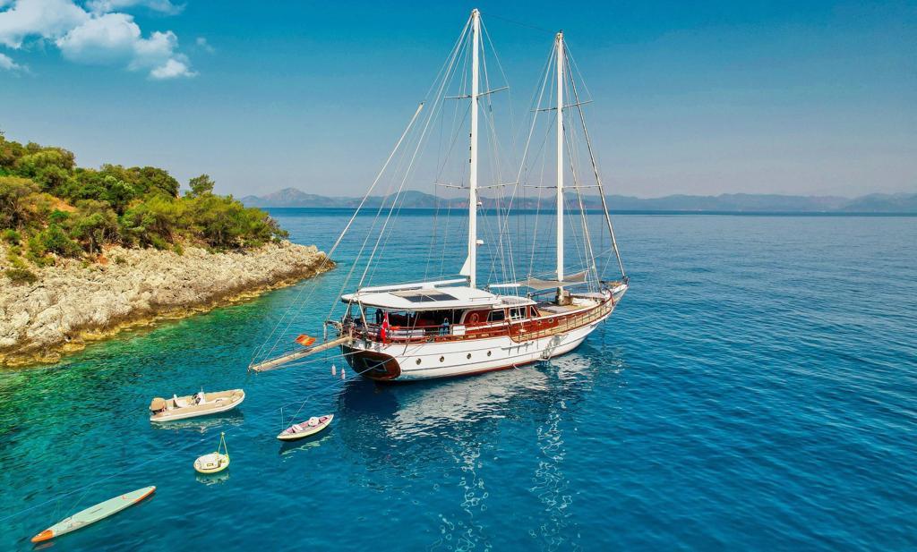 Traditional wooden gulet yacht anchored in crystal clear turquoise Mediterranean bay with rocky coastline