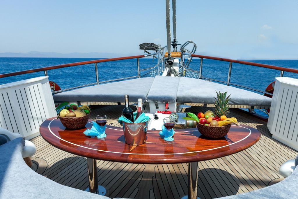 circular wooden dining table set with wine bottles, glasses, fruit bowls and pineapple on yacht deck