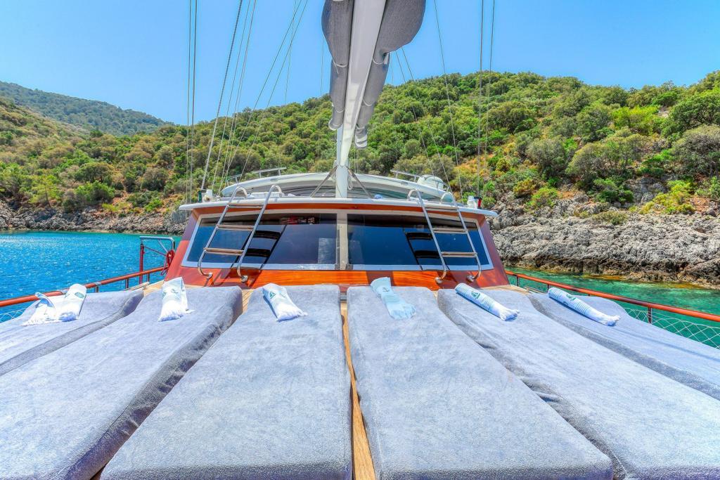 bow sun deck with gray cushioned loungers and white pillows overlooking turquoise bay