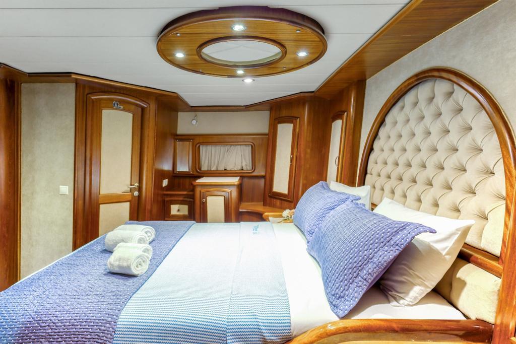 yacht cabin interior with white bedding, cream tufted headboard, wood paneling and circular ceiling feature