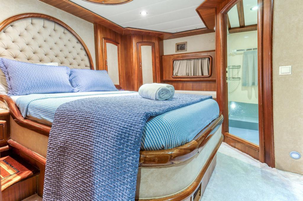 yacht guest cabin featuring curved bed with blue textured bedding and ensuite bathroom entrance
