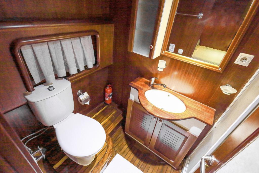 compact yacht bathroom featuring toilet, wooden wash basin counter, mirror and teak flooring
