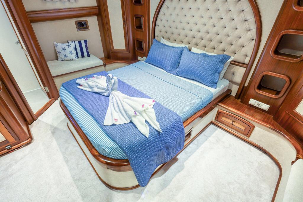 yacht guest cabin featuring double bed with blue bedding, single berth, and cream upholstered curved headboard