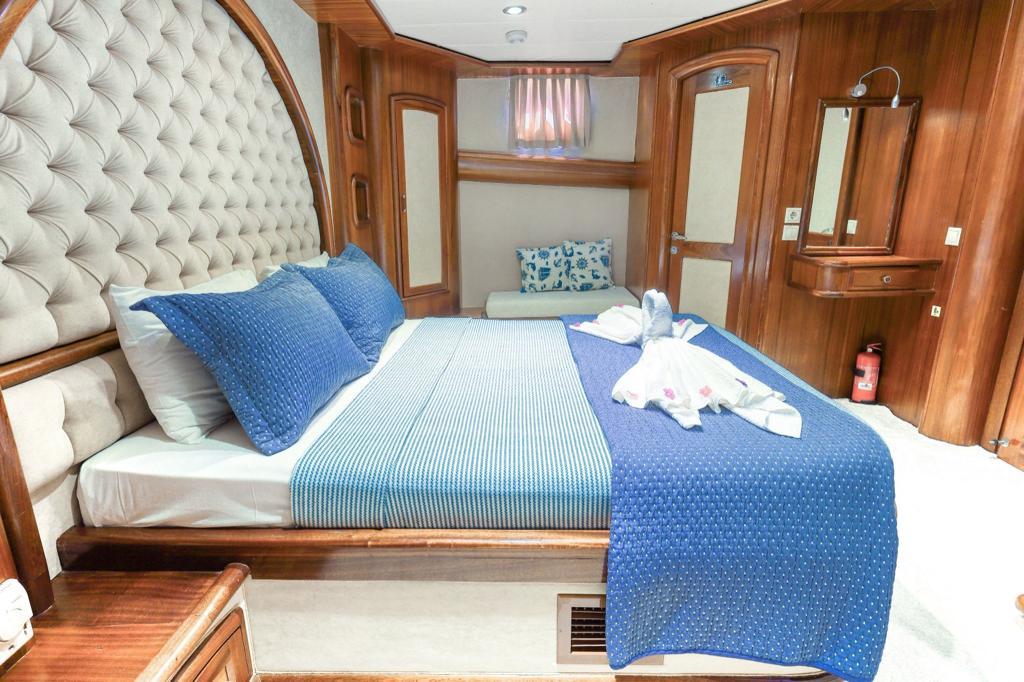yacht guest cabin featuring white tufted leather headboard, blue bedding, and wooden cabinetry