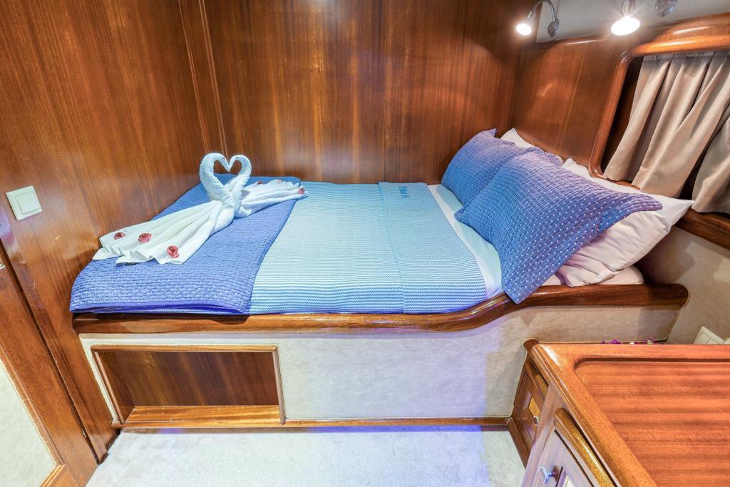 yacht cabin interior with double bed, blue bedding, towel swans and wood paneling