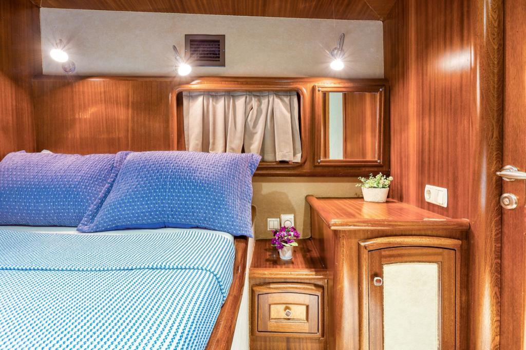 yacht cabin with blue striped bedding, wooden built-in furniture and storage compartments