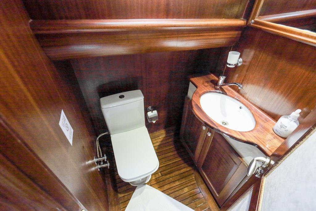 yacht bathroom with white toilet, wooden vanity sink, and teak flooring
