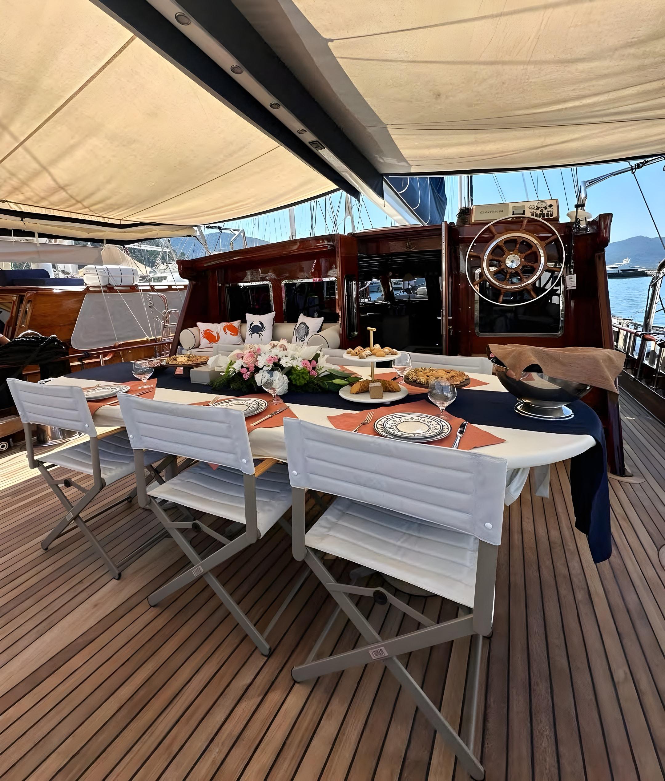 Luxury gulet aft deck dining table set with decorated plates, wine glasses, floral centrepiece and food platters under cream canvas awning