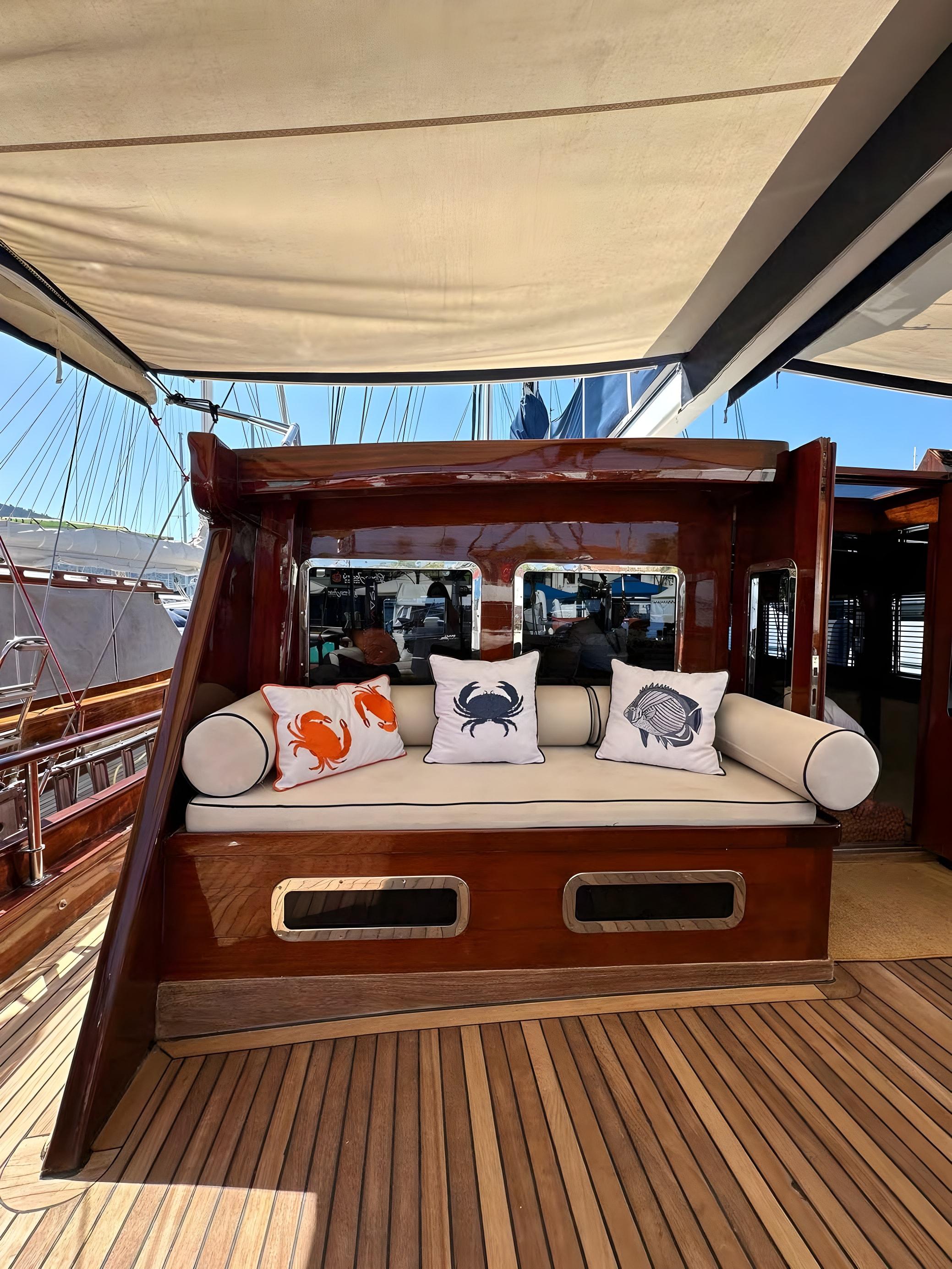 Gulet aft deck built-in daybed with cream cushions and marine-embroidered throw pillows under canvas awning