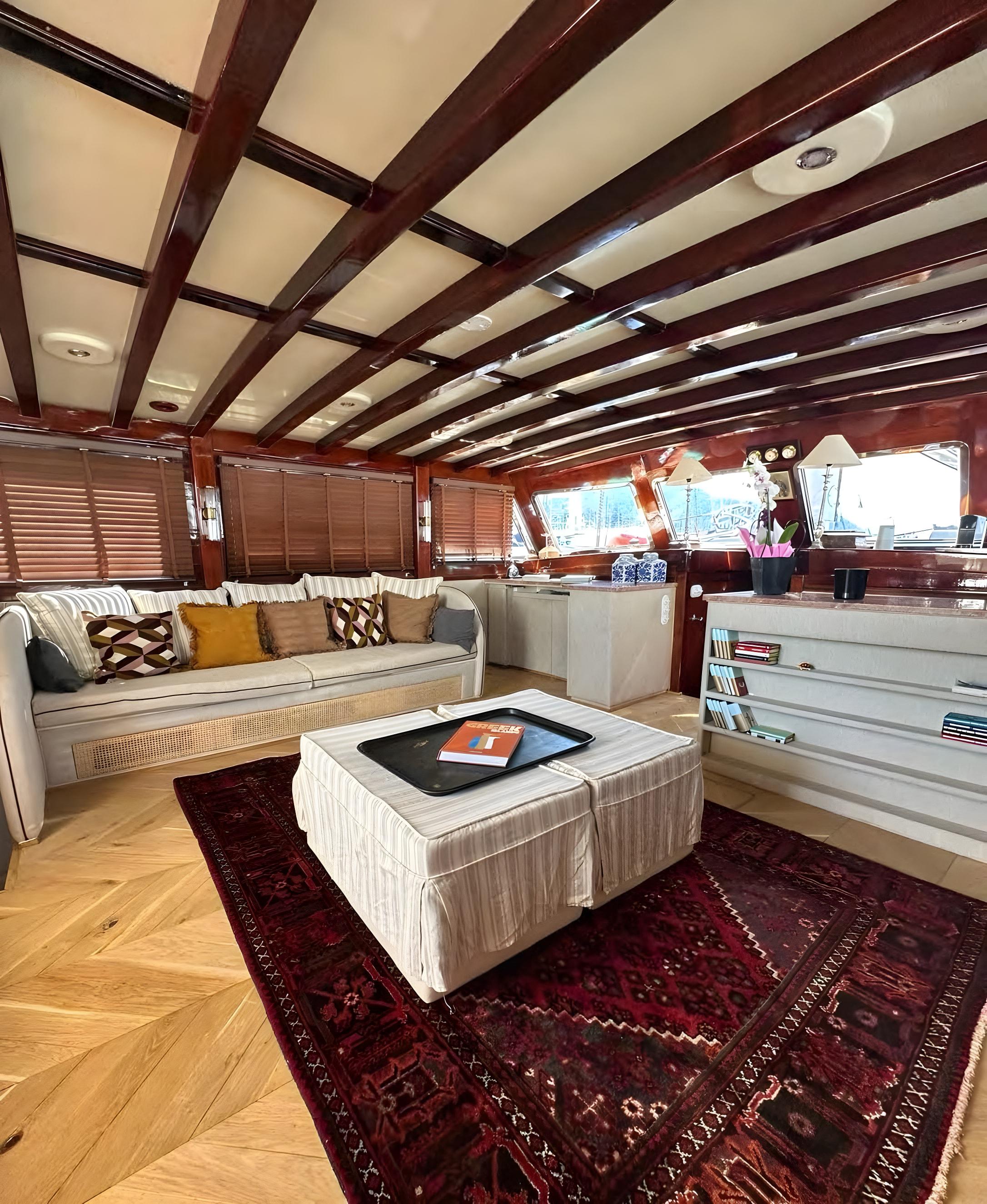 Gulet interior saloon with cream sofa, striped ottoman, red Persian rug and dark mahogany beam ceiling