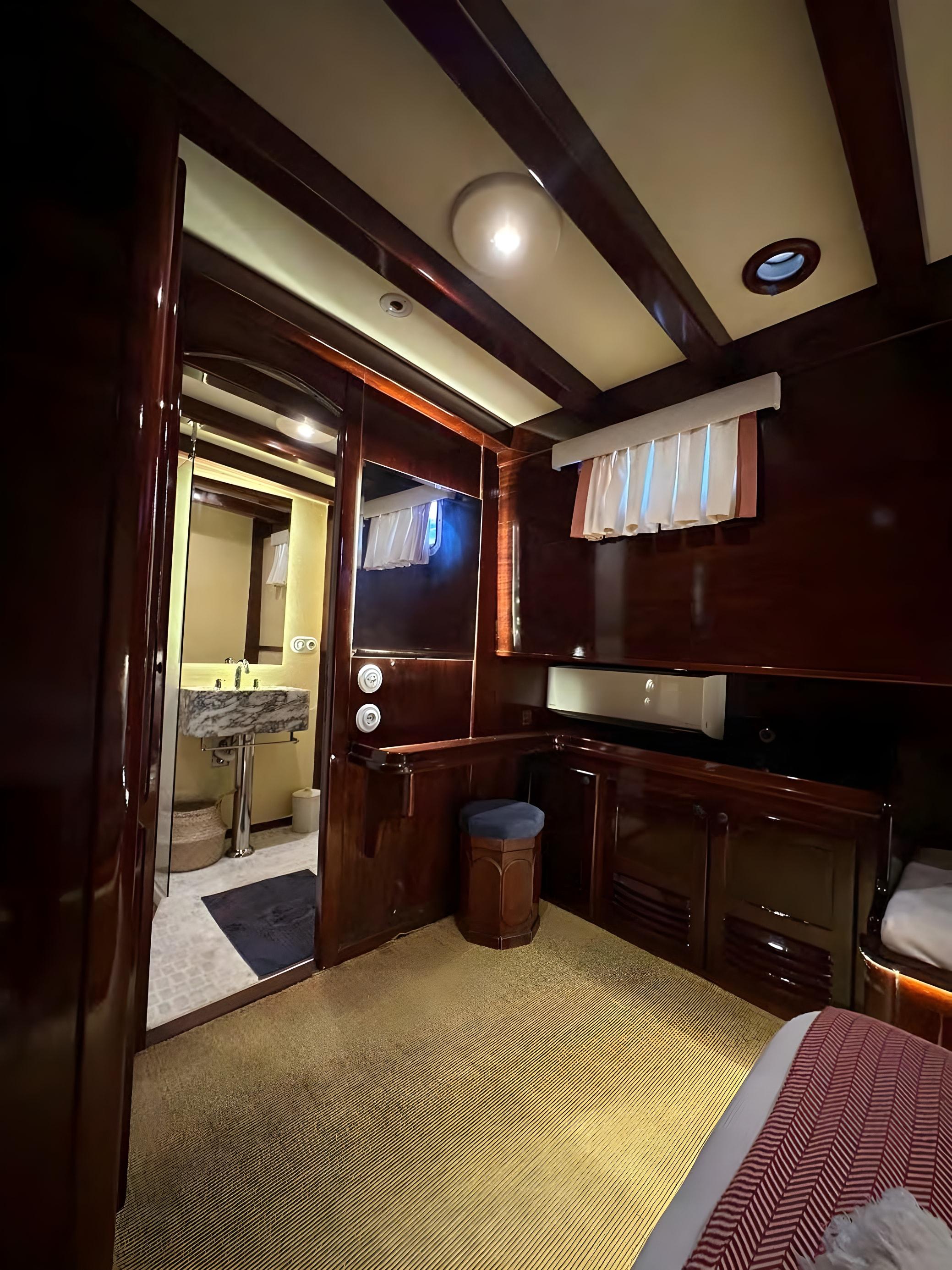 Gulet guest cabin with dark mahogany panelling, built-in cabinetry, vanity area and en-suite bathroom with marble sink