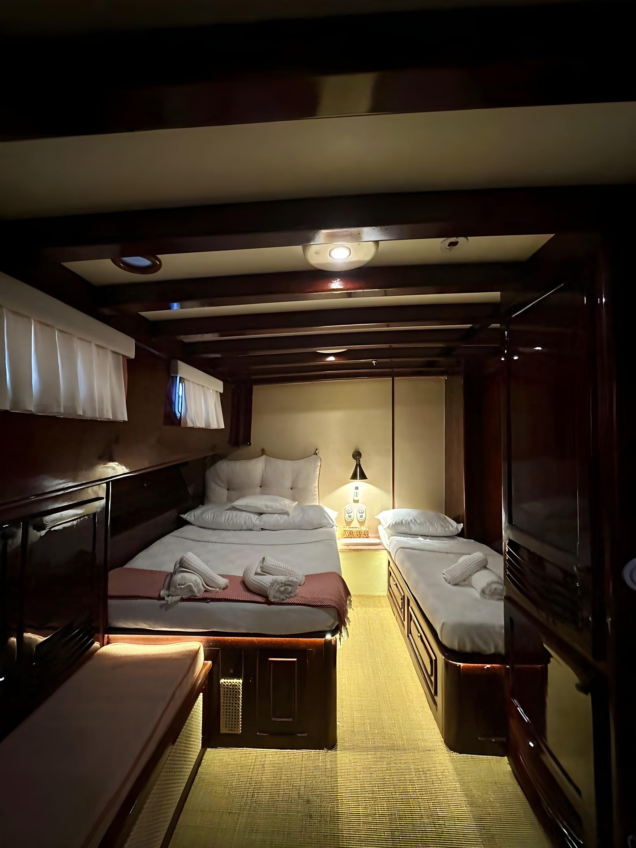 Gulet cabin with double bed, single berth, towel sculptures, wall lamp and wooden beamed ceiling
