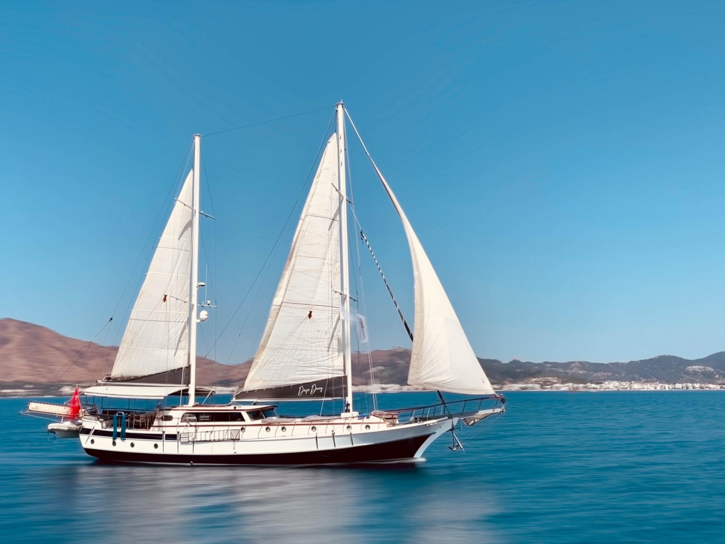 Traditional Turkish gulet named Doga Deniz sailing with three full white sails on calm turquoise water