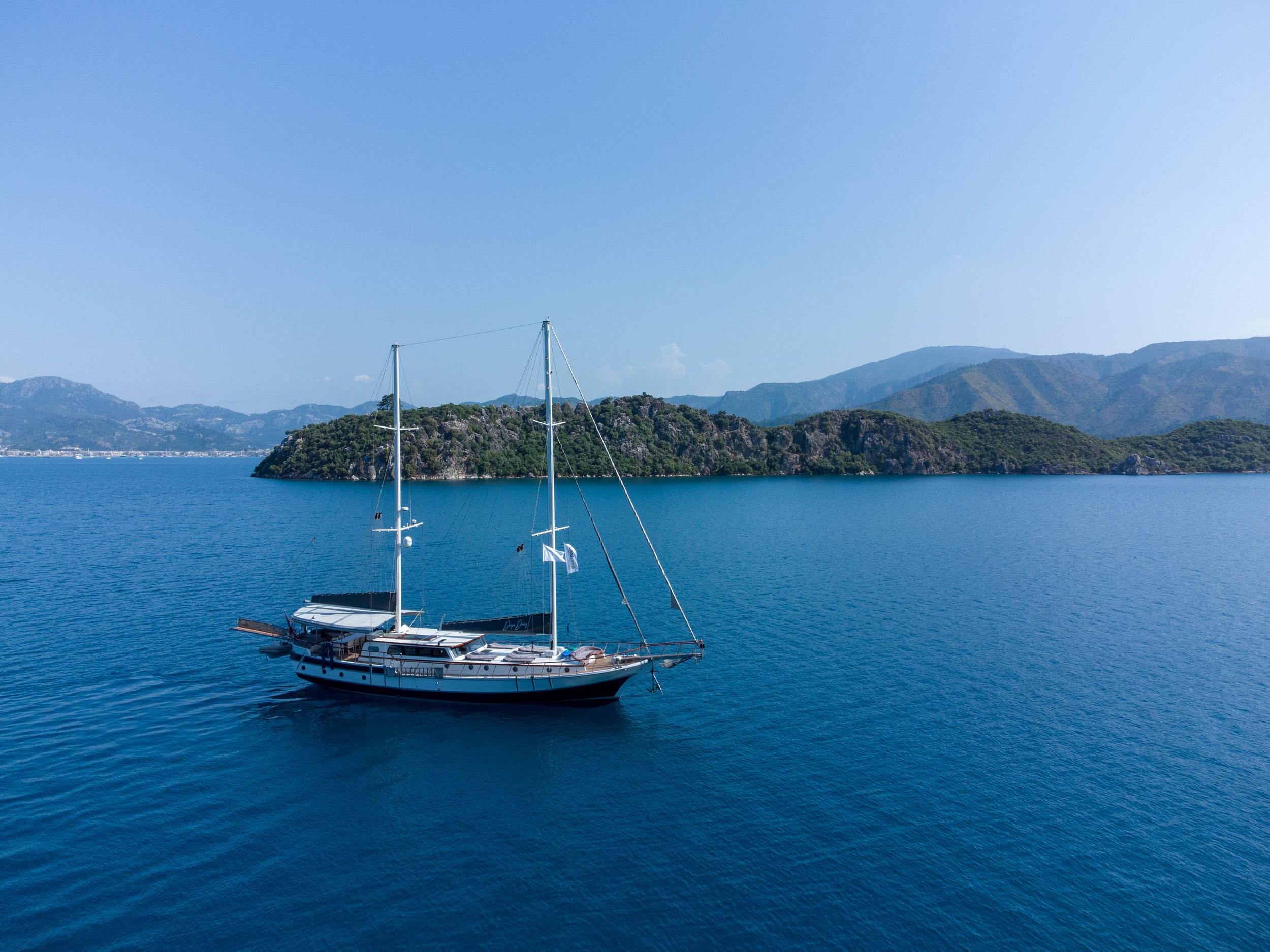 Aerial drone view of a classic two-masted gulet anchored in deep blue Turkish waters with rocky green islands behind