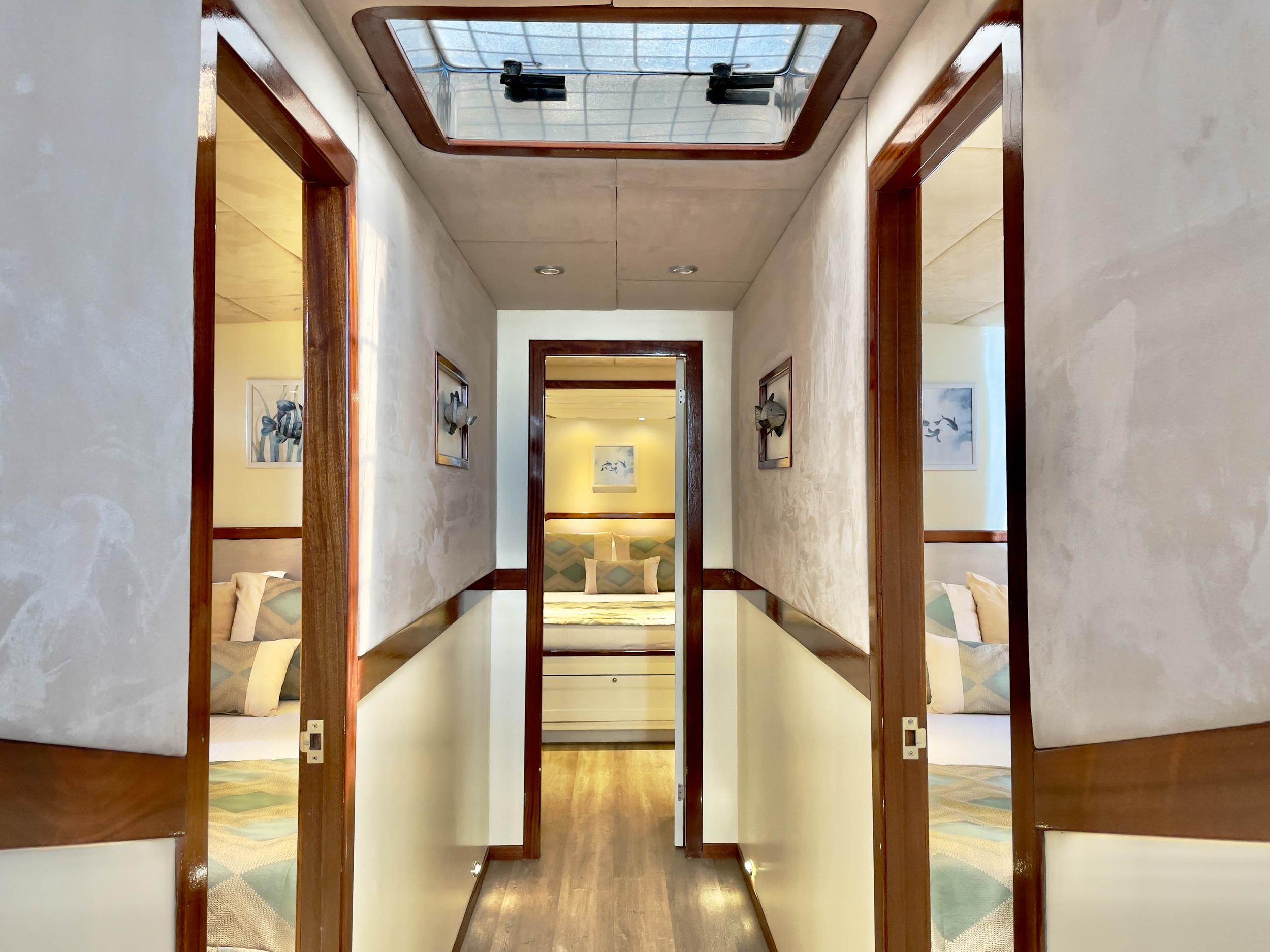 Gulet interior corridor with teak-framed doors opening to double cabin, overhead skylight, and marine artwork on walls