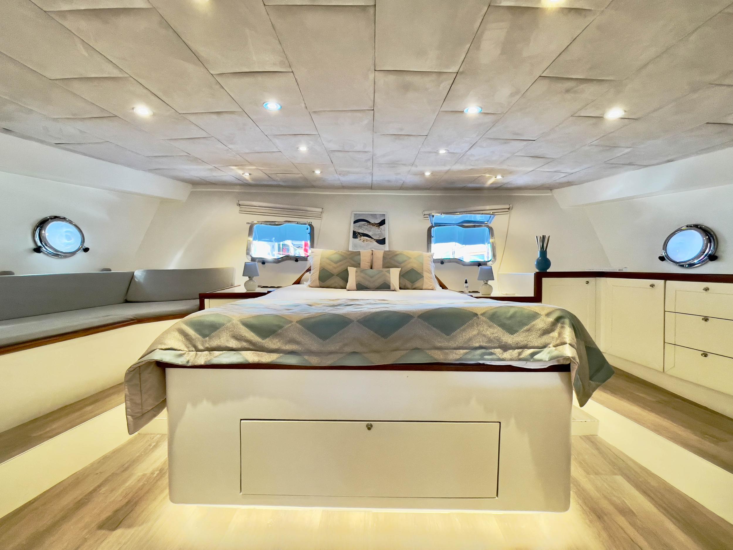 Spacious master cabin with king-size bed, upholstered ceiling panels, twin portholes, and built-in storage drawers