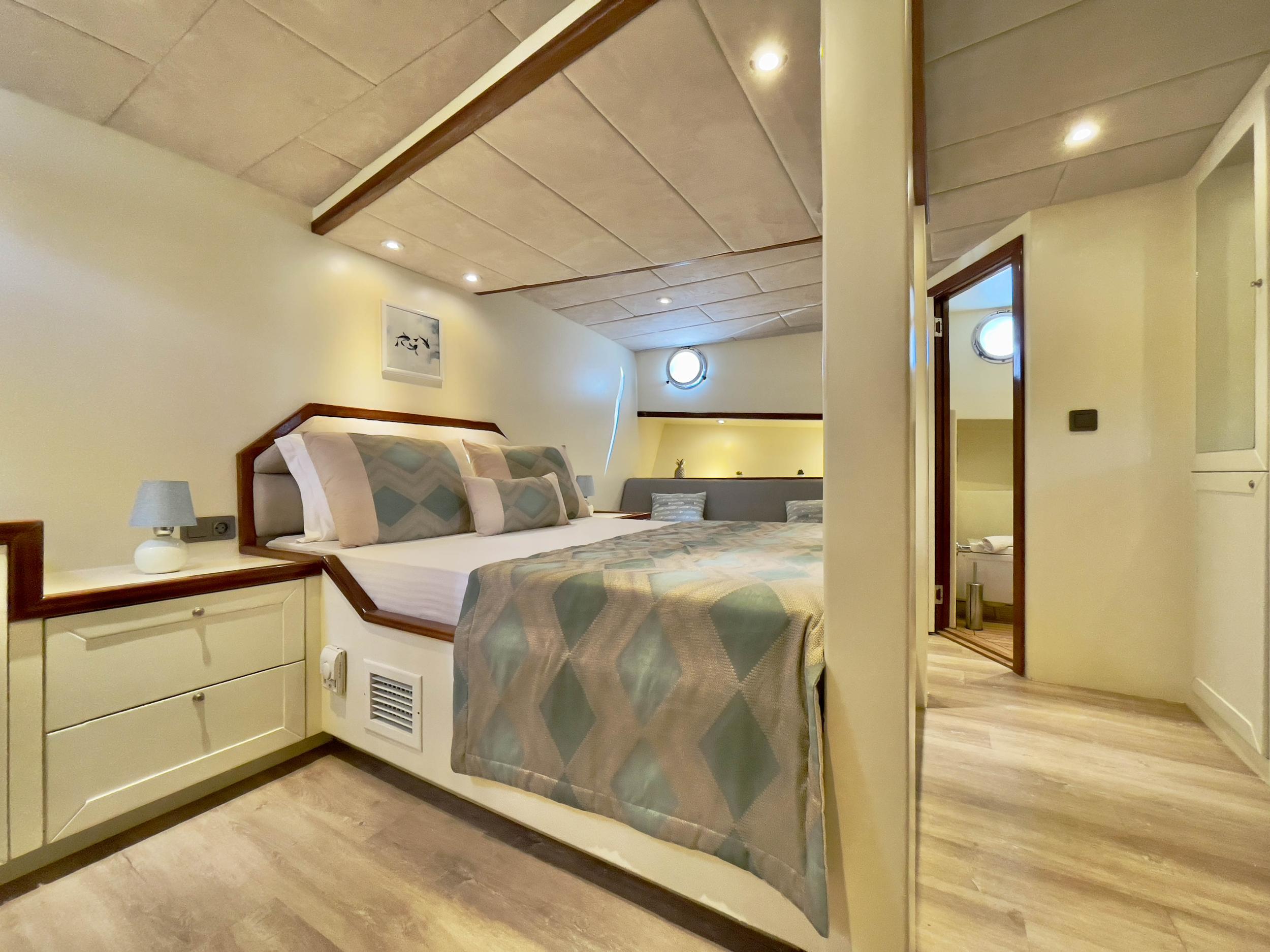 Gulet double cabin with diamond-patterned bedding, wood-trimmed headboard, bedside drawers, and en-suite bathroom doorway visible